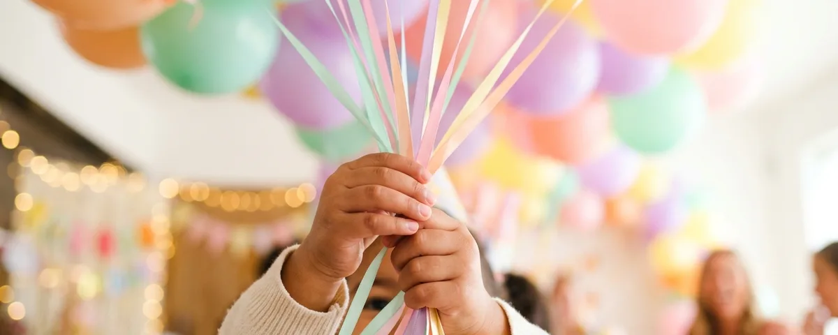 A child holding a bunch of pastel balloons by their ribbons at a party