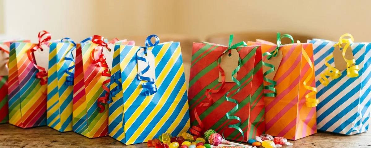 Striped party bags lined up on a table with sweets in front of them