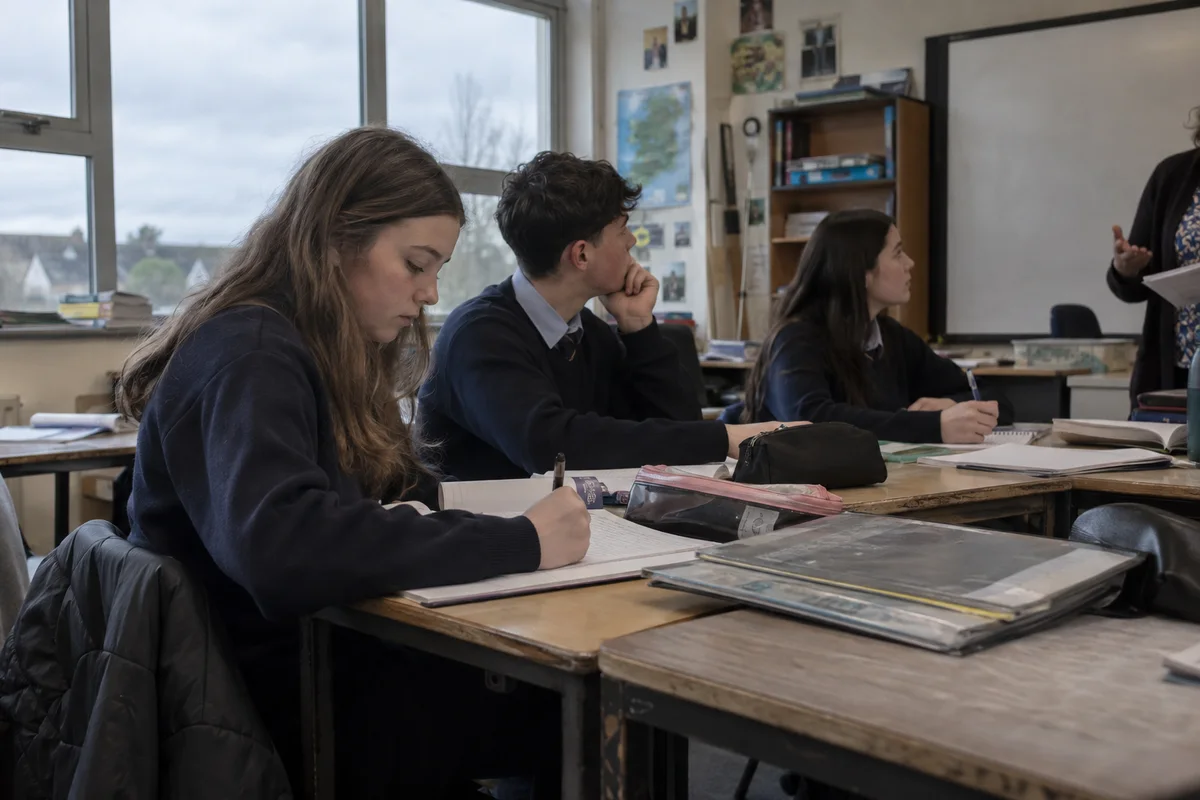 Secondary school students writing and listening in a classroom